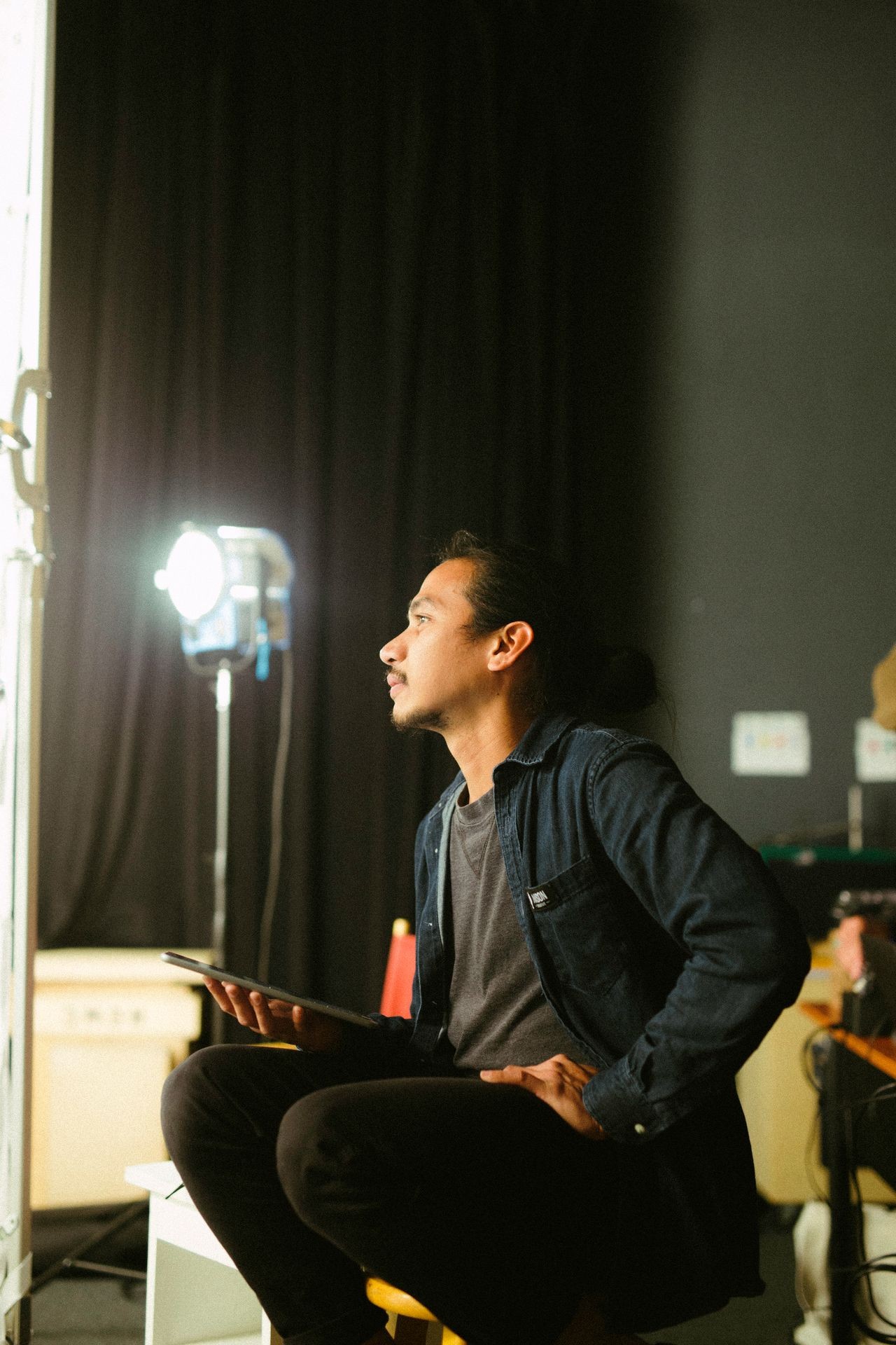Person sitting in a dimly lit room holding a tablet, with studio lights in the background.
