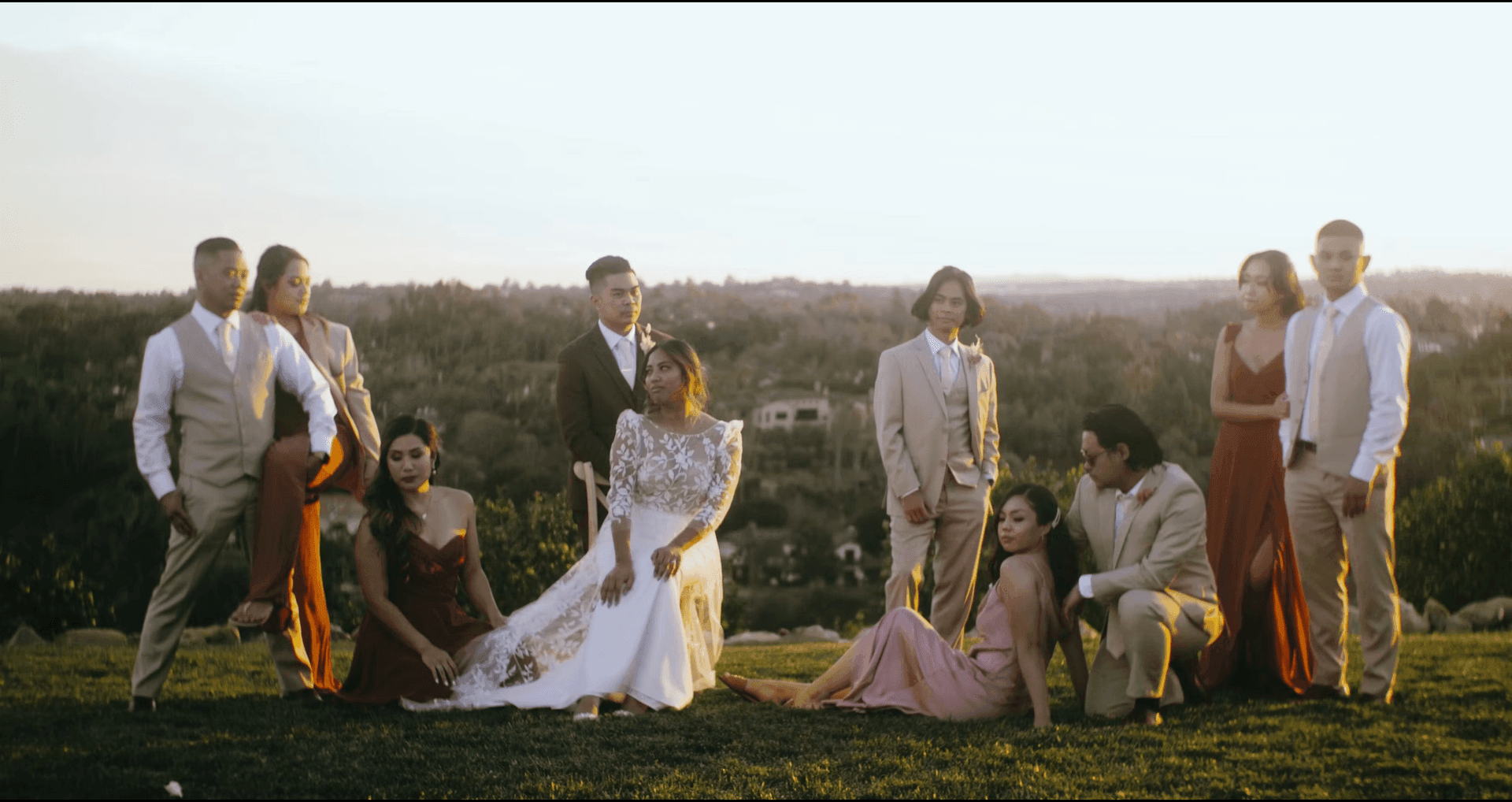 Group posing elegantly in formal attire on a grassy hillside at sunset.